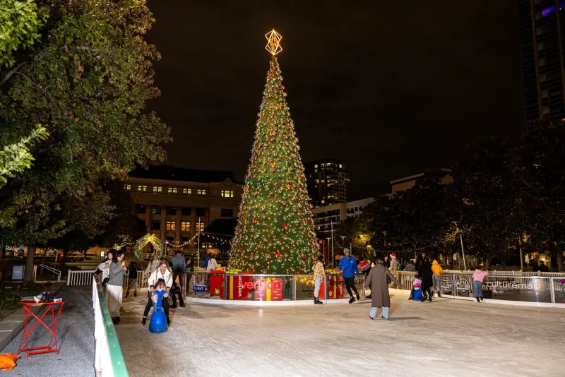 Wide nighttime view of skaters circling the City Rink Christmas tree