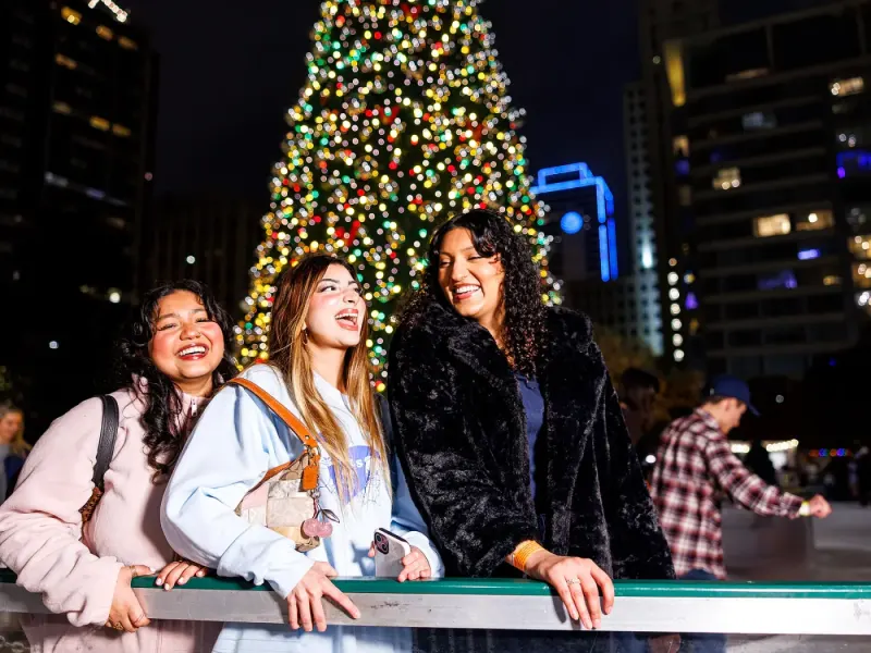 Friends laughing together beside the rink and Christmas tree