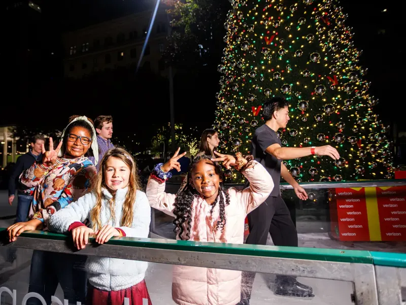 Children smiling beside the rink and illuminated Christmas tree